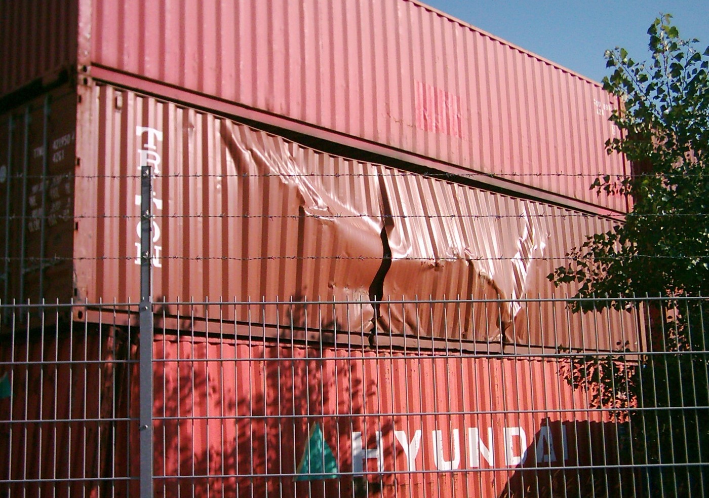 A shipping container with buckled exterior panels and a visible tear